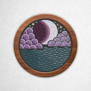 May include: A circular cross-stitch embroidery piece framed in wood, featuring a pixelated night scene with a large moon, purple swirling clouds, and a dark teal wavy ocean surface under a starry sky, all set against a textured white background.