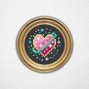 Pode incluir: Um design de ponto cruz emoldurado com um coração rosa com um anel de planeta verde-azulado sobre um fundo preto. O coração é adornado com pontos cruzados brancos e rodeado por estrelas e pontos coloridos. A moldura é dourada.