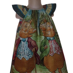 May include: A children's dress featuring a whimsical illustration of two pigs in coats and vests, with a matching bow. The dress has a green and yellow floral pattern on the sleeves and neckline. The pigs are depicted in a forest setting.