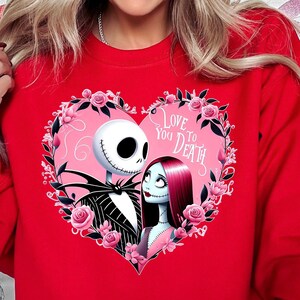 Może przedstawiać: Czerwona bluza z nadrukiem r&oacute;żowego serca z Jackiem Skellingtonem i Sally z filmu Koszmar przed świętami. Tekst w sercu brzmi "Love You To Death."