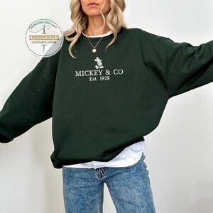 Puede incluir: Una sudadera verde oscuro con un Mickey Mouse bordado en blanco y el texto "MICKEY & CO Est. 1928".