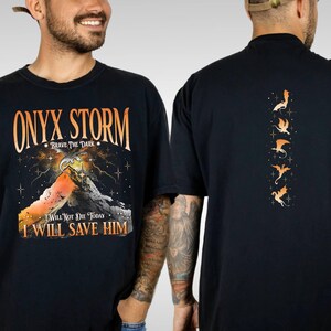 May include: Black t-shirt with a mountain scene and the text "ONYX STORM - BRAVE THE DARK - I WILL NOT DIE TODAY I WILL SAVE HIM". The back of the shirt has a vertical row of five orange dragons.
