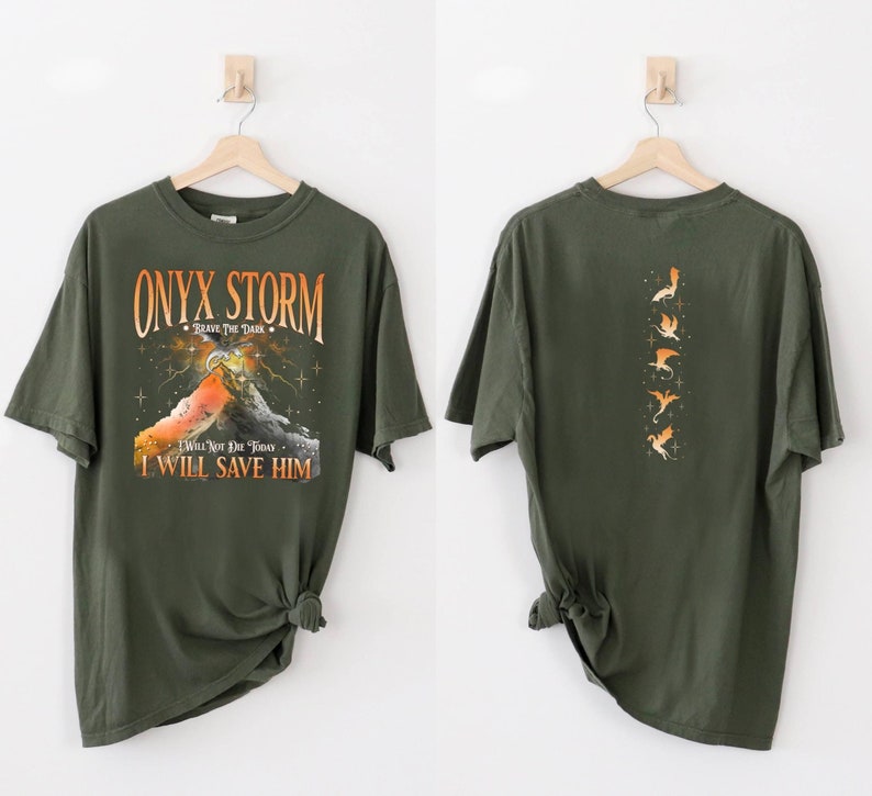 May include: A green t-shirt with a graphic print of a mountain and the text "ONYX STORM - BRAVE THE DARK - I WILL NOT DIE TODAY - I WILL SAVE HIM". The back of the shirt has a graphic print of a series of flying dragons.