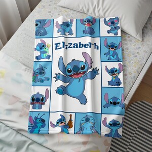 Peut inclure: Une couverture bleue et blanche repr&eacute;sentant le personnage Stitch de Lilo & Stitch. La couverture pr&eacute;sente un motif quadrill&eacute; avec diverses images de Stitch et le nom "Elizabeth" en texte bleu. La couverture est sur un lit avec un oreiller blanc.