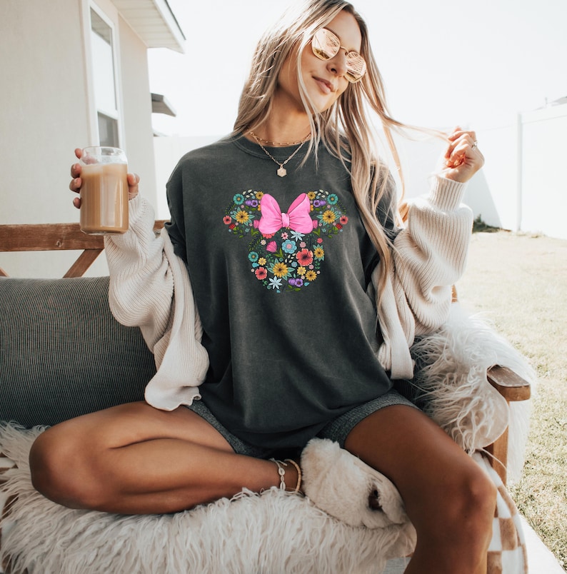 Puede incluir: Sudadera gris oscuro con un dise&ntilde;o floral de Minnie Mouse. El dise&ntilde;o incluye un lazo rosa y flores coloridas. La sudadera es de corte holgado y adecuada para uso casual.