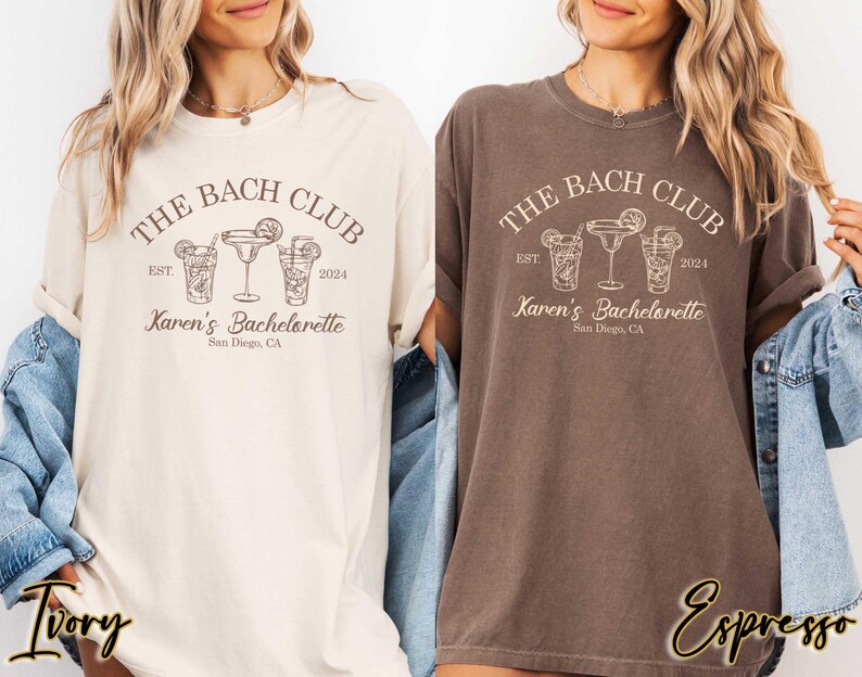 May include: Two t-shirts with a brown and white design. The text on the shirts reads "The Bach Club Est. 2024 Karen's Bachelorette San Diego, CA". One shirt is ivory and the other is espresso.