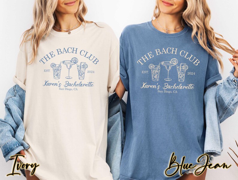 May include: Two t-shirts with the text "The Bach Club Est 2024 Karen's Bachelorette San Diego, CA" and a graphic of three cocktail glasses. One shirt is ivory and the other is blue jean.