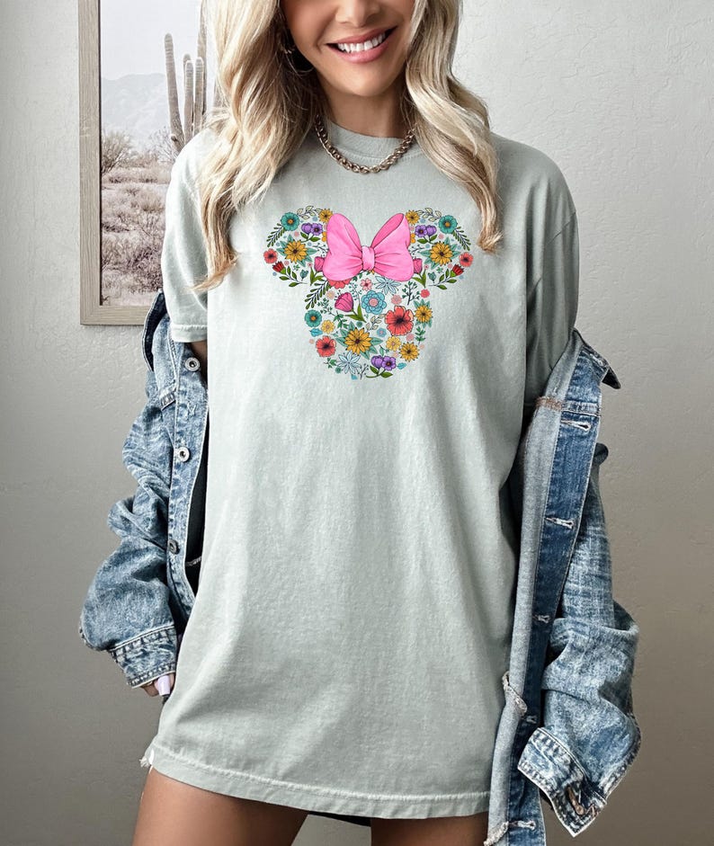 Puede incluir: Camiseta verde claro con un dise&ntilde;o floral de Minnie Mouse. El dise&ntilde;o incluye un lazo rosa y flores coloridas en forma de la cabeza de Minnie Mouse. La camiseta es de estilo casual y c&oacute;modo.