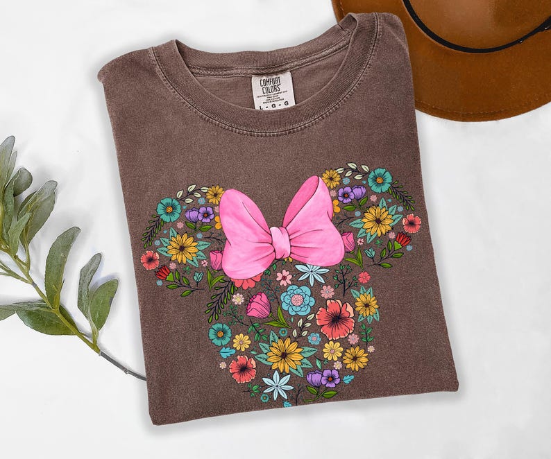 Puede incluir: Camiseta Comfort Colors marr&oacute;n con un dise&ntilde;o floral de Minnie Mouse. El dise&ntilde;o incluye un gran lazo rosa y flores coloridas en tonos amarillos, azules, morados y rojos. La camiseta es talla L-G-G.