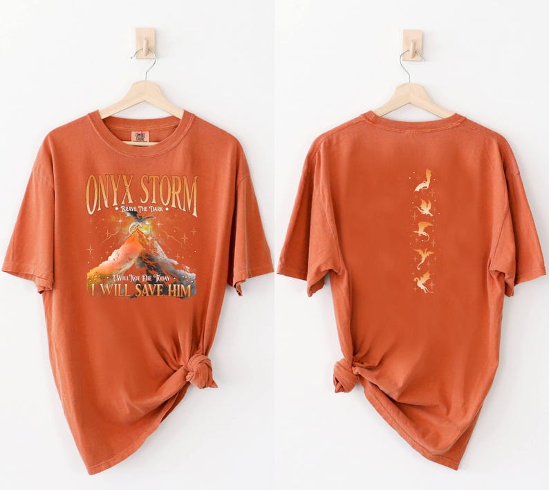 May include: A burnt orange t-shirt with a graphic print of a mountain and the text "ONYX STORM - Brave The Dark - I Will Not Let You Down - I Will Save Him". The back of the shirt has a graphic print of five flying birds.