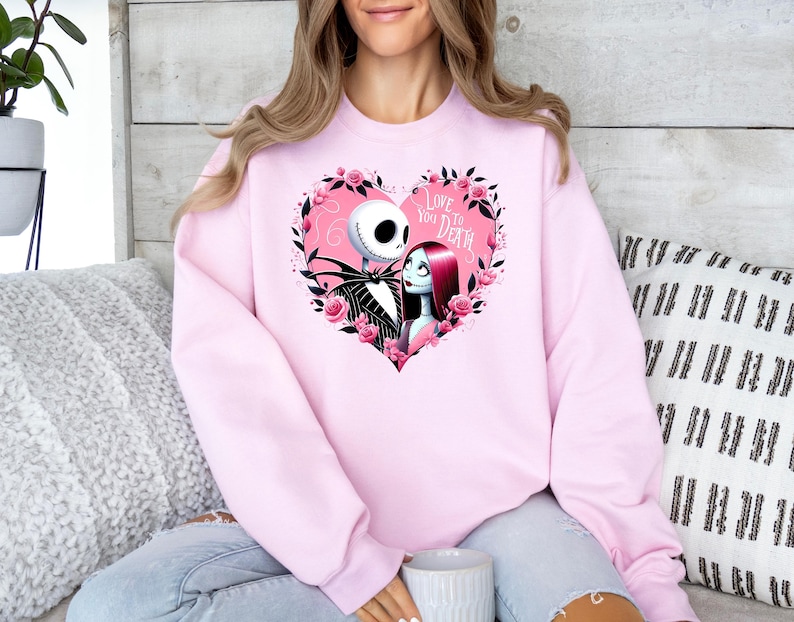 Może przedstawiać: R&oacute;żowa bluza z nadrukiem Jacka Skellingtona i Sally z filmu Koszmar przed świętami. Nadruk przedstawia serce z tekstem "Love You To Death".