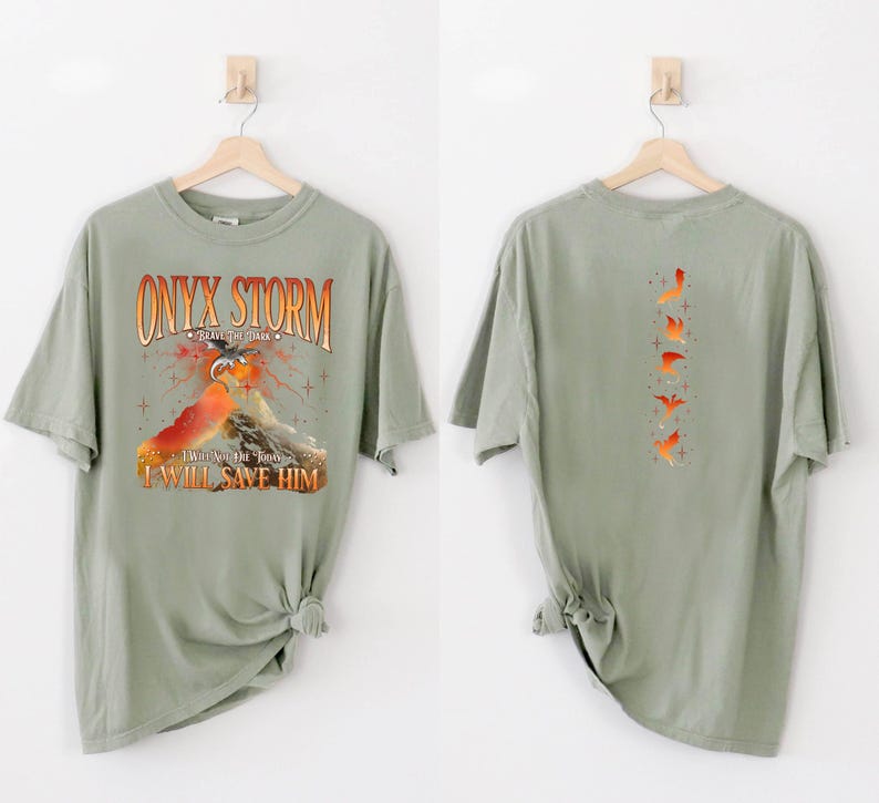 May include: A sage green t-shirt with a graphic print of a dragon and a mountain. The text "ONYX STORM" is printed in orange and black. The text "I WILL SAVE HIM" is printed in orange. The back of the shirt has a graphic print of five orange birds.
