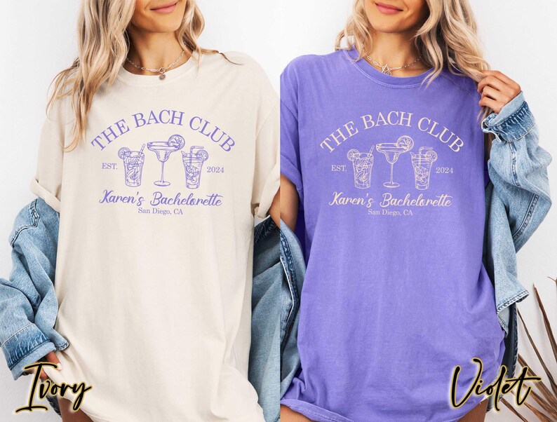 May include: Two t-shirts with a purple design that says "The Bach Club" with a date and the text "Karen's Bachelorette" with a location. The t-shirts are in the colors ivory and violet.
