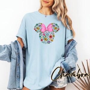 Puede incluir: Camiseta azul claro con un dise&ntilde;o floral de Minnie Mouse. El dise&ntilde;o incluye un lazo rosa y un arreglo floral con la forma de la cabeza de Minnie Mouse. La camiseta es de un material suave y c&oacute;modo.