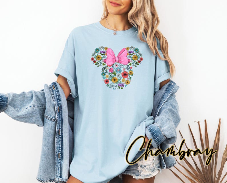 Puede incluir: Camiseta azul claro con un dise&ntilde;o floral de Minnie Mouse. El dise&ntilde;o incluye un lazo rosa y un arreglo floral con la forma de la cabeza de Minnie Mouse. La camiseta es de un material suave y c&oacute;modo.