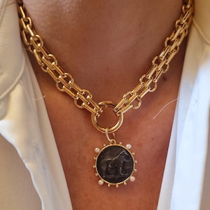 May include: A gold chain necklace with a large round pendant featuring a black and white image of a horse. The pendant is surrounded by small white pearls.