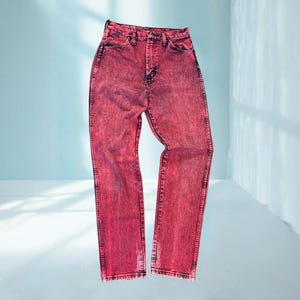 May include: A pair of acid-wash red denim jeans. The jeans have a high waist and a straight leg cut. The denim is a vibrant red with darker red accents, and the jeans are displayed against a light blue background.