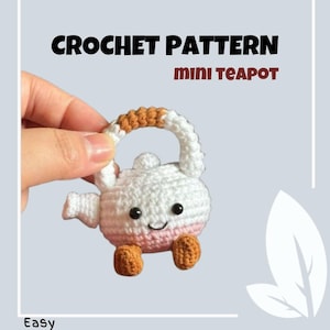 Puede incluir: Una mini tetera de ganchillo con cuerpo blanco, base rosa y asa y pies marrones. La tetera tiene una cara sonriente con ojos negros. El texto "CROCHET PATTERN mini TEAPOT" se muestra encima de la tetera, con la palabra "Easy" en la parte inferior.