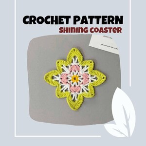 May include: A handmade crochet coaster in a flower shape. The coaster features a yellow-green outer layer, white and pink petals, and a yellow center. The text "CROCHET PATTERN SHINING COASTER" is at the top.