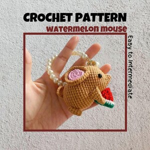 Op de afbeelding: Haakpatroon voor een watermeloenmuis amigurumi. De muis is bruin met een roze oor en houdt een rood en groen watermeloenplak vast. Het patroon wordt beschreven als gemakkelijk tot middelmatig.