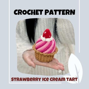 Könnte beinhalten: Häkelanleitung für eine Erdbeer-Eis-Tarte. Die Tarte ist rosa und weiß mit einer braunen Kruste und einer roten Erdbeere oben drauf.