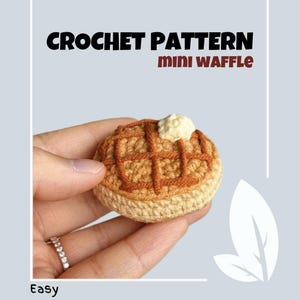 Puede incluir: Patrón de crochet para una mini wafla, con un trozo de mantequilla tejido en la parte superior. La wafla es marrón y beige, y la mantequilla es blanca. El patrón se describe como fácil.