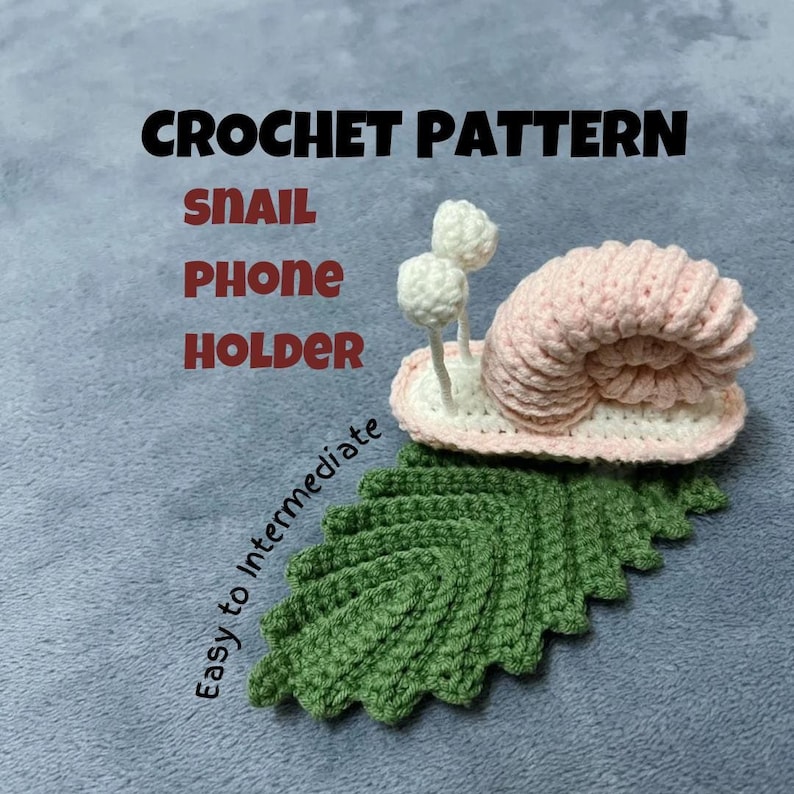 May include: Crochet pattern for a snail phone holder. The snail is pink with white eyes and is sitting on a green leaf. The text "CROCHET PATTERN" is at the top of the image, and the text "SNAIL PHONE HOLDER" is below it. The text "Easy to Intermediate" is written diagonally on the left side of the image.