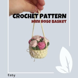 May include: Crochet pattern for a mini rose basket. The basket is cream colored and filled with pink and white crocheted roses. The basket has a handle and is hanging from a hand.