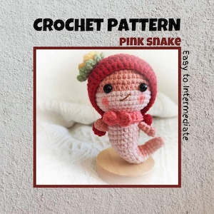 May include: Crochet pattern for a pink snake amigurumi toy. The snake is wearing a red crocheted hat with a flower on top. The pattern is labeled "Easy to Intermediate".
