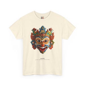 May include: Cream-colored t-shirt featuring a colorful Barong mask design. The mask has a detailed, ornate design with red, blue, yellow, and green accents. The word "BARONG" is printed below the mask.