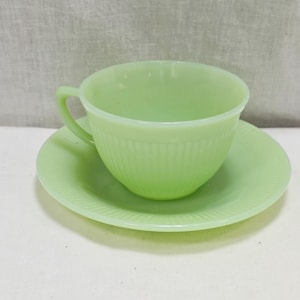 Puede incluir: Un juego de taza y platillo verde claro. La taza tiene un asa y detalles acanalados verticales. El platillo tiene un diseño acanalado a juego. El juego está hecho de vidrio translúcido, similar al jade.