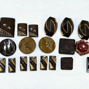 May include: Assortment of brown, gold, and burgundy buttons with various geometric and abstract designs.