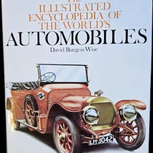 Könnte beinhalten: Ein gebundenes Buch mit dem Titel The Illustrated Encyclopedia of the World's Automobiles von David Burgess Wise. Das weiße Cover zeigt ein braunes Oldtimer-Automobil mit dem Kennzeichen LH-3042 und über 4000 Einträgen.