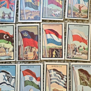 Op de afbeelding: Een verzameling van 12 vintage verzamelkaarten met vlaggen uit verschillende landen. Elke kaart toont een kleurrijke illustratie van de vlag, de naam van het land en een klein tafereel dat een bezienswaardigheid of symbool uit dat land voorstelt.