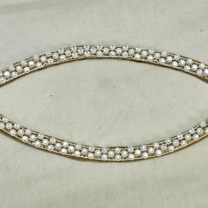 May include: A gold-toned, oval-shaped, rhinestone trim with a double row of clear rhinestones.