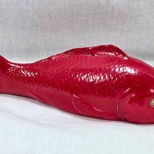 Può includere: Una statuetta di pesce in ceramica rosso vivo con una superficie dettagliata e testurizzata. Il pesce ha la bocca leggermente aperta e un occhio nero.