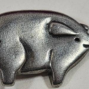 Könnte beinhalten: Eine silberfarbene Schweinchenfigur. Das Schweinchen steht auf allen vieren und hat einen leicht gebogenen Schwanz.