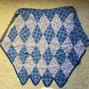 May include: A blue and white patchwork apron with a diamond pattern. The apron has a scalloped edge and a tie.