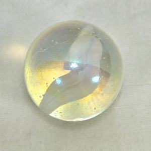 Può includere: Un marmo di vetro trasparente e iridescente con un motivo a spirale di bianco e giallo.
