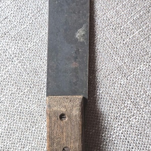 Peut inclure: Une lame métallique rectangulaire vintage avec un manche en bois. La lame est sombre et usée, tandis que le manche est brun clair. Deux vis fixent le manche à la lame. Cet outil est probablement utilisé pour couper ou façonner.