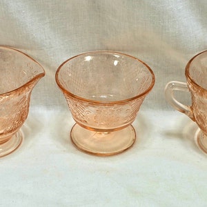 May include: Three vintage pink glass sugar bowls with a delicate floral pattern. The bowls have a footed base and are perfect for serving sugar or other condiments.