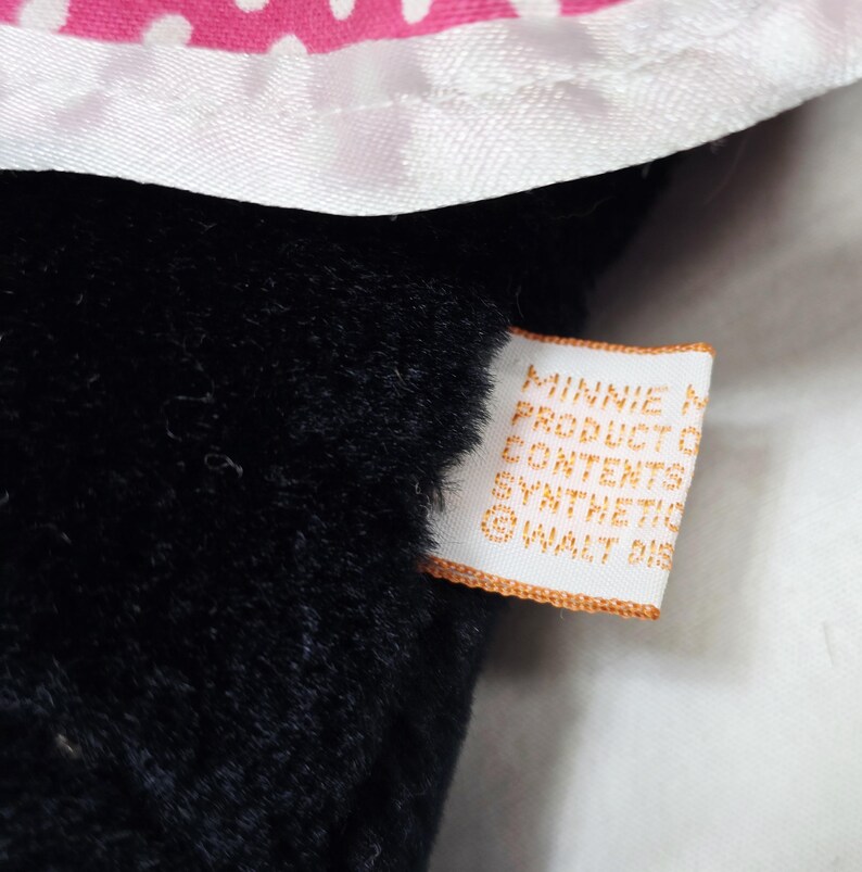 May include: Close-up of a black plush toy with a white and pink polka dot bow. A tag with the text "MINNIE MOUSE PRODUCT OF CONTENTS SYNTHETIC &copy; WALT DIS" is attached to the toy.