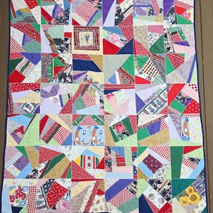 May include: A rectangular patchwork quilt featuring a variety of multi-colored fabric scraps in geometric shapes. The quilt includes diverse patterns such as floral prints, red and white gingham, polka dots, and cartoon hot dog illustrations.
