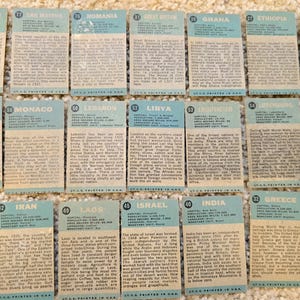 Op de afbeelding: Een verzameling van 16 vintage verzamelkaarten met informatie over verschillende landen over de hele wereld. Elke kaart heeft een blauwe achtergrond met witte tekst en een nummer in de linkerbovenhoek. De kaarten zijn gerangschikt in vier rijen van vier.