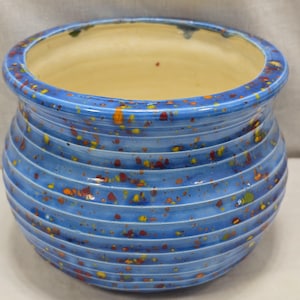 Peut inclure: Un pot en céramique bleu avec un glaçage moucheté et un design côtelé. Le pot a une large ouverture et un fond arrondi.