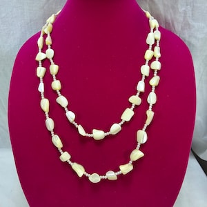 May include: A double strand necklace made of off-white, irregular shaped, shell beads. The necklace is displayed on a red velvet mannequin bust.