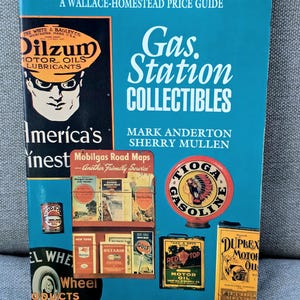 May include: A teal-colored book titled "Gas Station Collectibles" by Mark Anderton and Sherry Mullen. The cover features vintage gas station signs, oil cans, and Mobilgas road maps, with the Dilzum Motor Oils logo.
