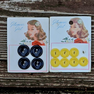 以下が含まれることがあります： 2つのヴィンテージボタンカード。1つのカードには4つのネイビーブルーのボタンがあり、もう1つのカードには8つの黄色のボタンがあります。各カードには、「Glamour Girl」というテキストが付いた女性のヴィンテージイラストがあります。