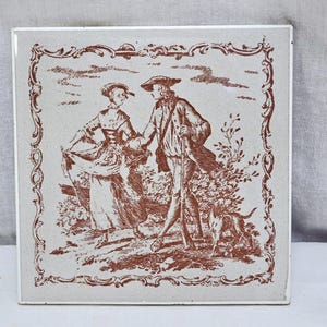 Può includere: Piastrella quadrata in ceramica con un'illustrazione color seppia di una coppia e un cane. La coppia indossa abiti d'epoca e la piastrella ha un bordo decorativo. Misura circa 15 cm x 15 cm.