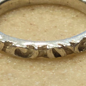 May include: A silver band ring with a textured design. The band is decorated with a repeating pattern of small, raised bumps.